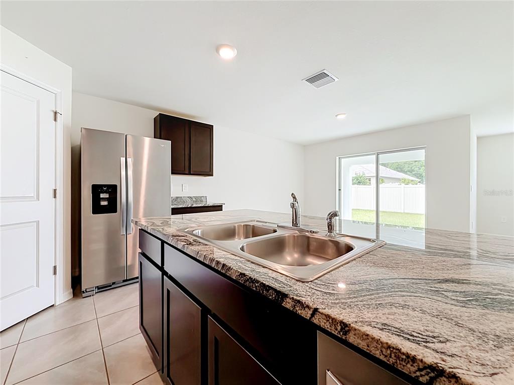 A kitchen features dark wood cabinets, granite countertops, a double sink, and stainless steel appliances — 6698 SE 3RD LOOP, OCALA, FL