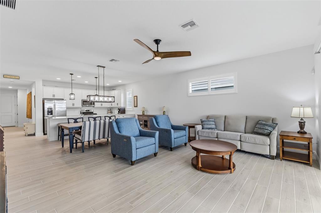 An open-concept living room and kitchen featuring light wood-look tile flooring and blue armchairs — 1003 WATERLINE COURT, SARASOTA, FL
