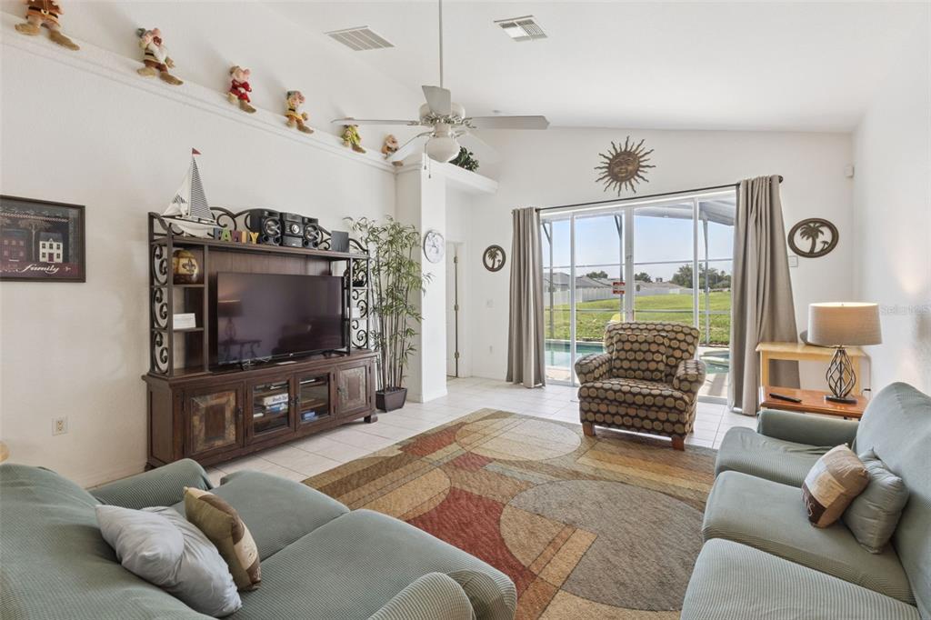 A living room features a television console, patterned area rug, armchair, and sliding glass doors — 121 VINE DRIVE, DAVENPORT, FL