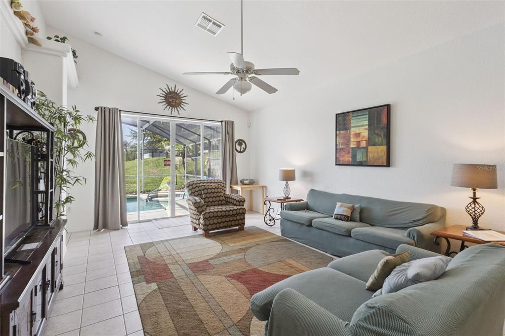 A living room features a vaulted ceiling, tile floors, a patterned rug, and sliding glass doors — 121 VINE DRIVE, DAVENPORT, FL