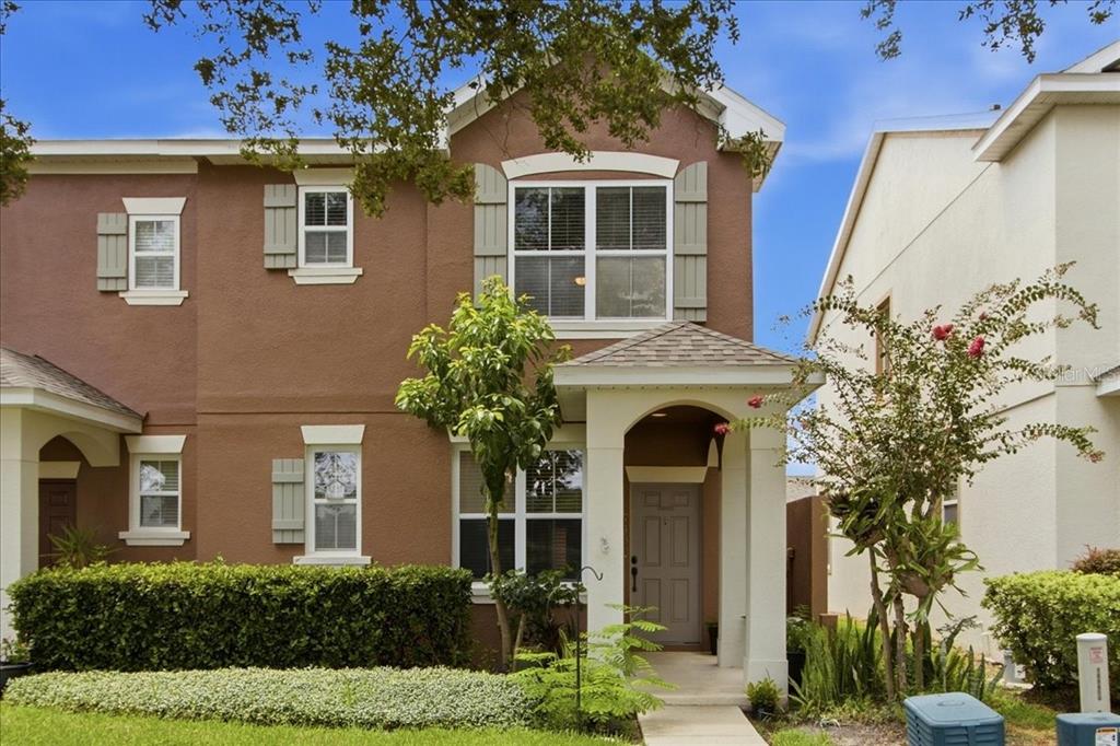 A two-story brown townhouse with a covered entryway, white trim, and a manicured hedge — 7430 BENTONSHIRE AVENUE, WINDERMERE, FL