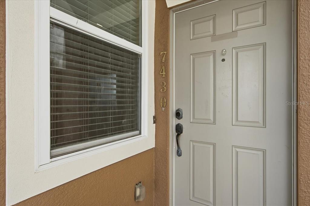 A light-colored front door with a handle set sits next to a window with blinds — 7430 BENTONSHIRE AVENUE, WINDERMERE, FL