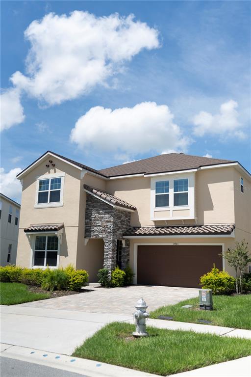 A two-story suburban house with tan stucco, stone accents, a brown garage, and a fire hydrant — 8981 AMELIA DOWNS TRAIL, KISSIMMEE, FL
