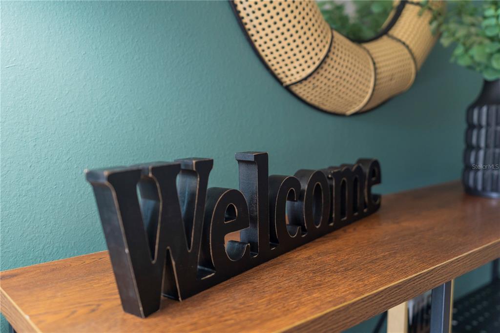 A black Welcome sign sits on a wooden console table against a teal wall — 8981 AMELIA DOWNS TRAIL, KISSIMMEE, FL