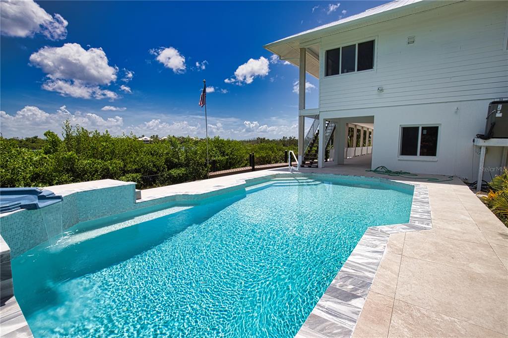 A swimming pool with a waterfall feature sits beside a white two-story house — 13064 VIA FLAVIA, PLACIDA, FL