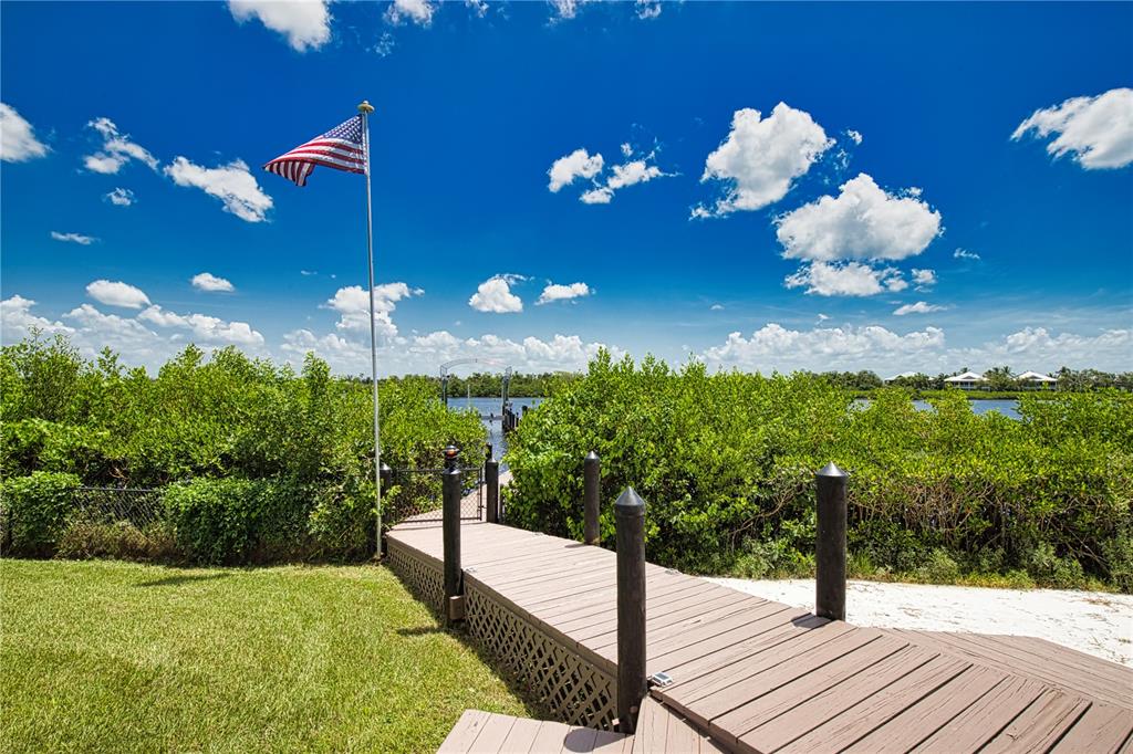 A wooden walkway leads through lush green bushes toward a boat dock and water — 13064 VIA FLAVIA, PLACIDA, FL