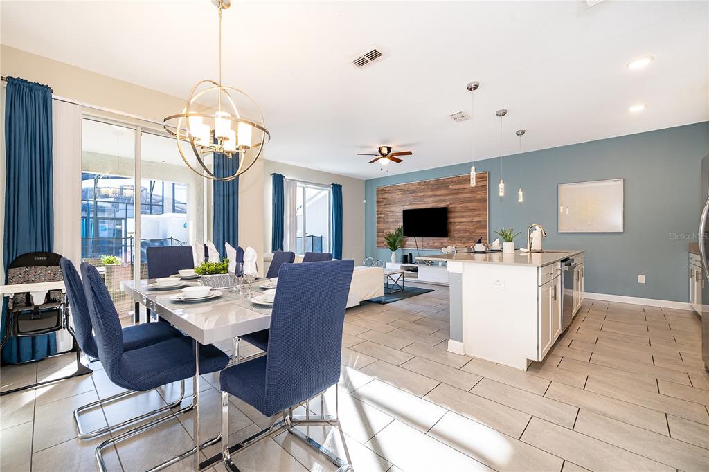 An open-concept dining area and kitchen feature blue chairs, a wood-paneled wall, and tile flooring — 4982 WINDERMERE AVENUE, KISSIMMEE, FL