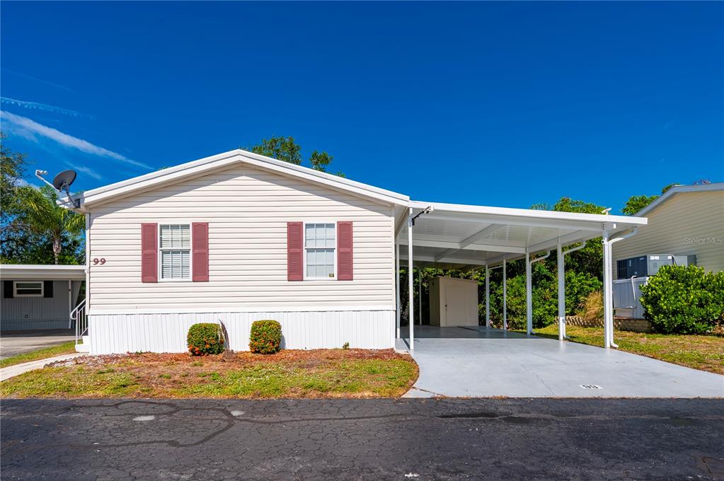 A single-story manufactured home features light siding, red shutters, and an attached carport — 24437 HARBORVIEW ROAD UNIT 99, PUNTA GORDA, FL