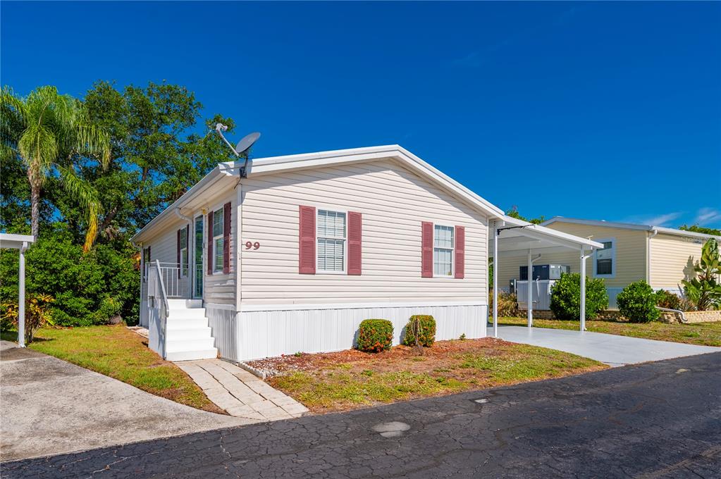 A light-colored manufactured home with red shutters, a carport, and white stairs — 24437 HARBORVIEW ROAD UNIT 99, PUNTA GORDA, FL