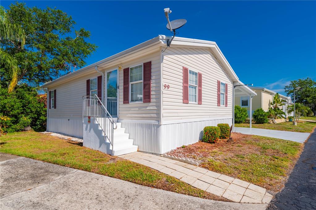 A single-story mobile home with beige siding, red shutters, and a white staircase — 24437 HARBORVIEW ROAD UNIT 99, PUNTA GORDA, FL