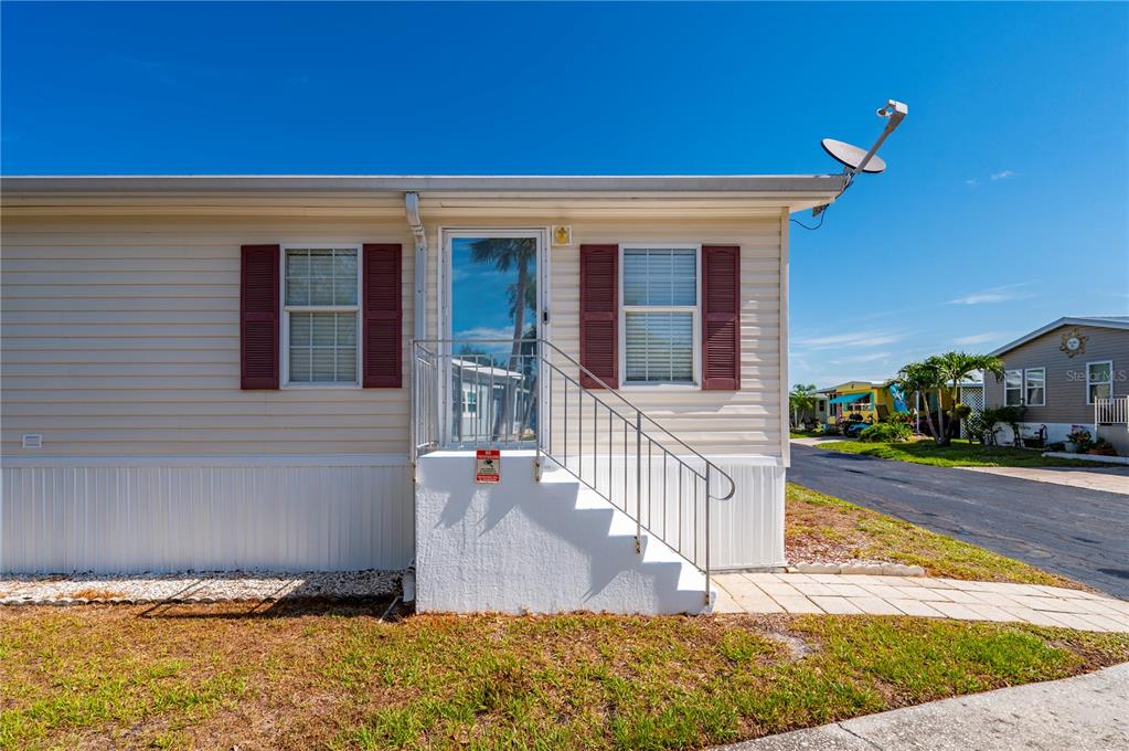 A tan mobile home exterior features a white staircase leading to a glass storm door — 24437 HARBORVIEW ROAD UNIT 99, PUNTA GORDA, FL