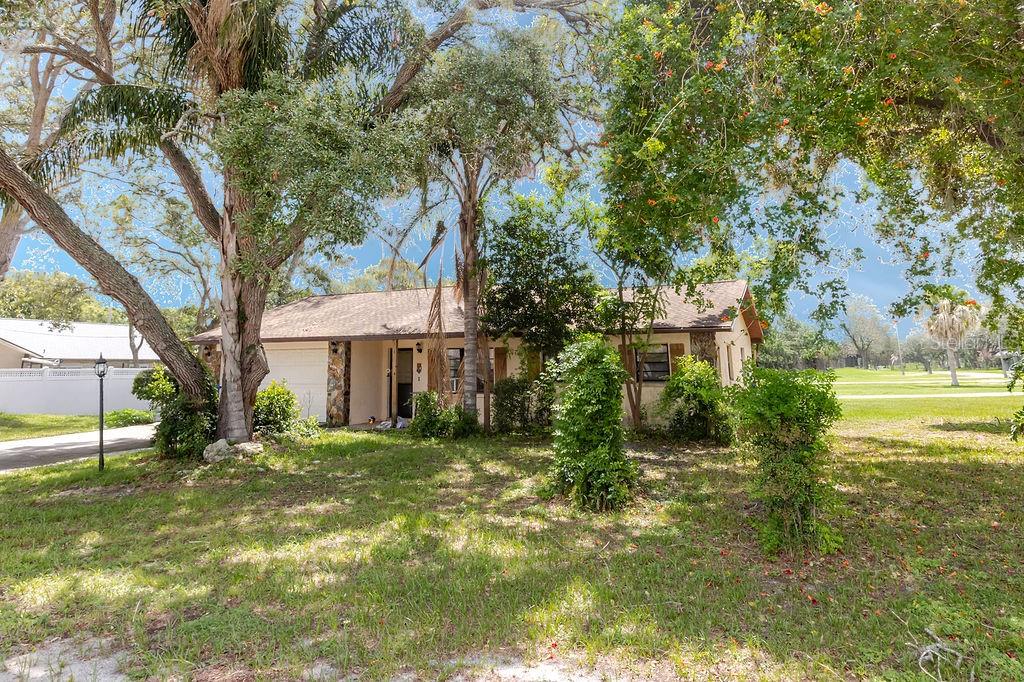 A single-story house with a garage and stone accents sits behind trees on a lawn — 1042 TRYON CIRCLE, SPRING HILL, FL
