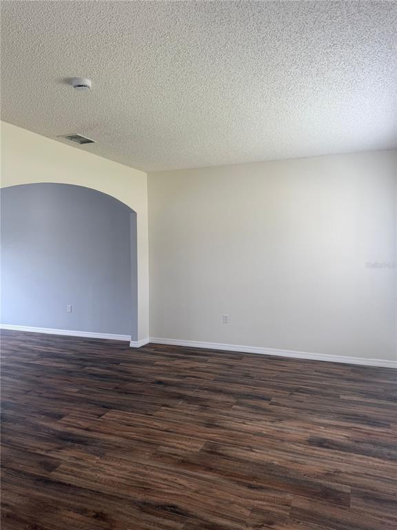 An empty room features wood-look flooring, a textured ceiling, and a large arched entryway — 401 MALLARD WAY, KISSIMMEE, FL