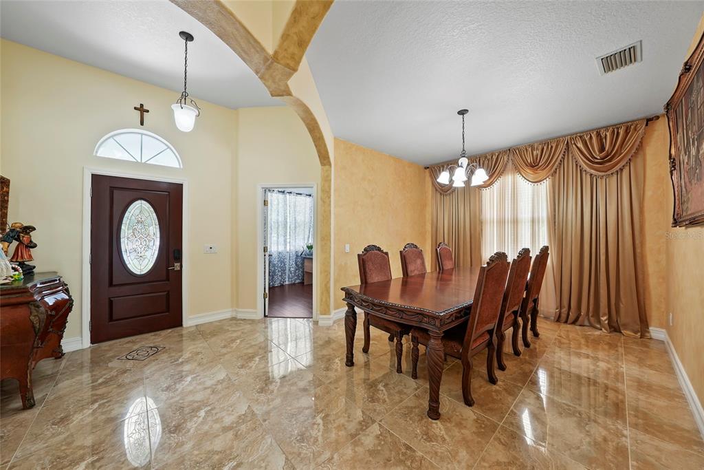 A dining room features a dark wood table, upholstered chairs, tile flooring, and gold curtains — 3817 LANGDRUM DRIVE, WESLEY CHAPEL, FL