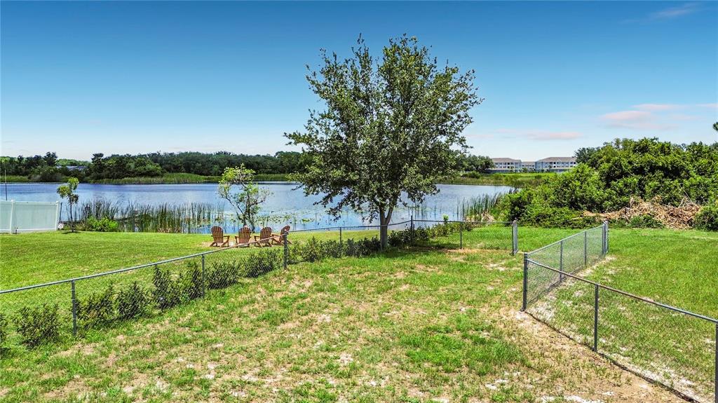 A grassy backyard features a chain-link fence, a large tree, and chairs overlooking a lake — 210 ROBBINS REST CIRCLE, DAVENPORT, FL