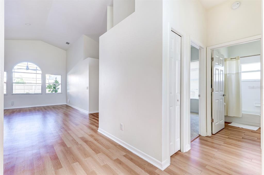 A bright living area with wood-look flooring leads to a hallway with a bathroom entrance — 10031 RIVER GLEN COURT, ORLANDO, FL