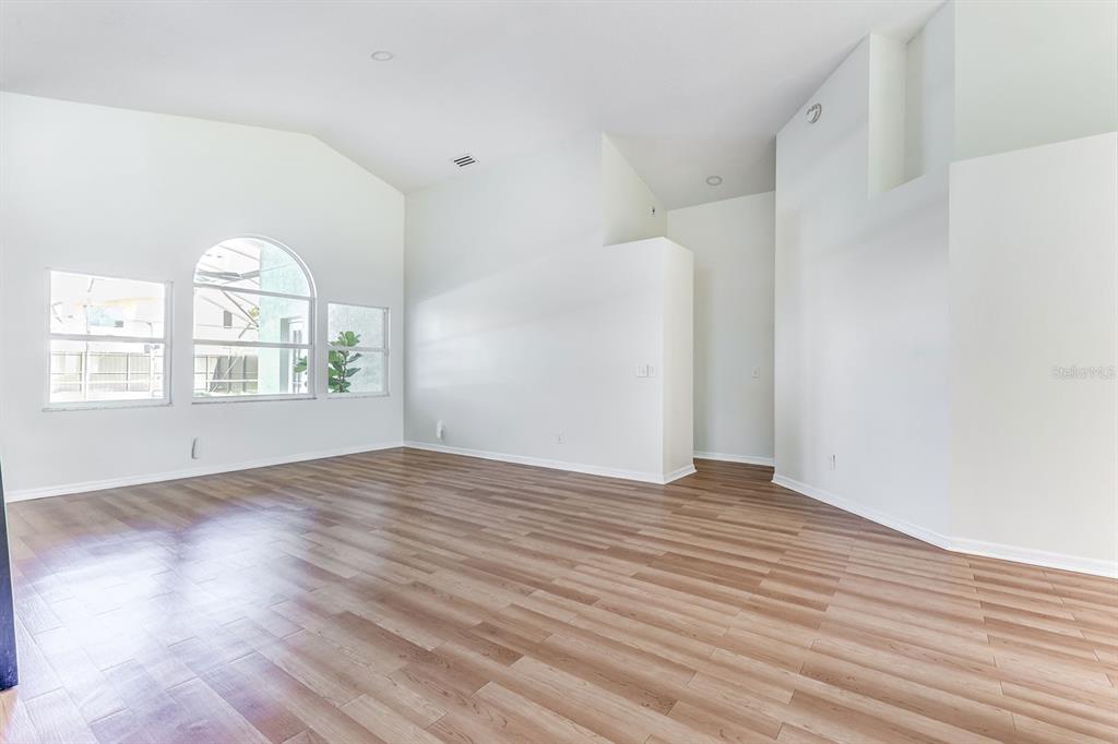 An empty living room features vaulted ceilings, light wood-look flooring, and large arched windows — 10031 RIVER GLEN COURT, ORLANDO, FL