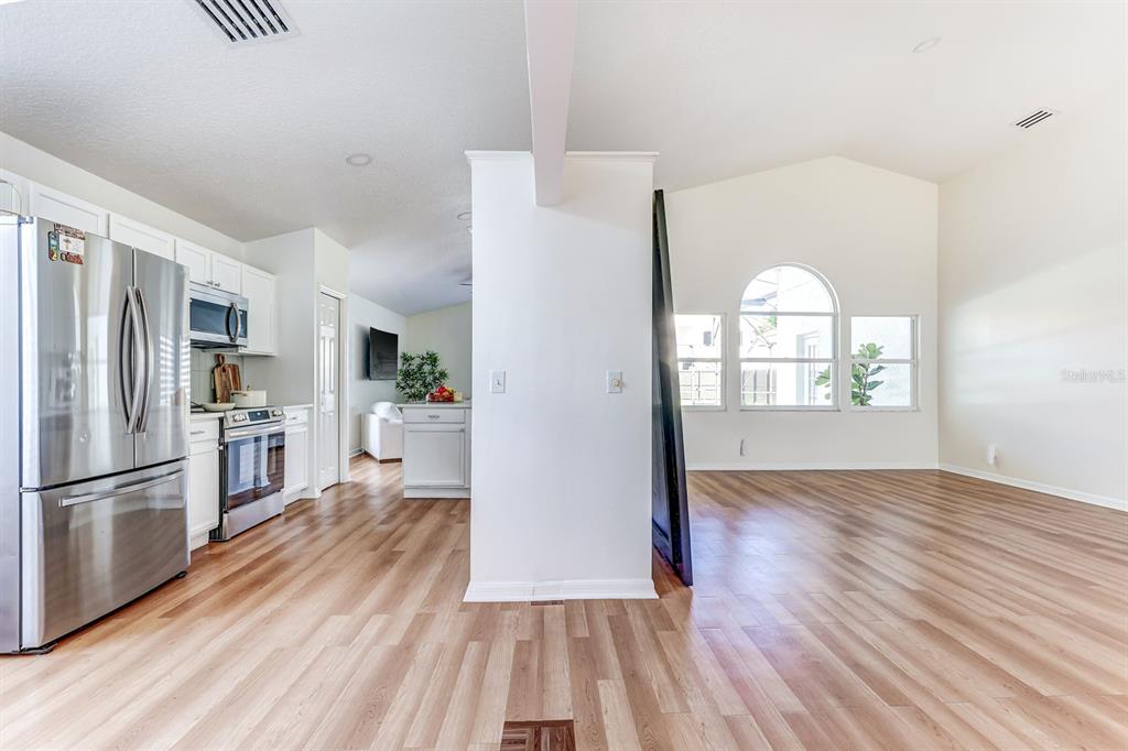 A kitchen with stainless steel appliances and wood-look flooring opens into a bright living area — 10031 RIVER GLEN COURT, ORLANDO, FL