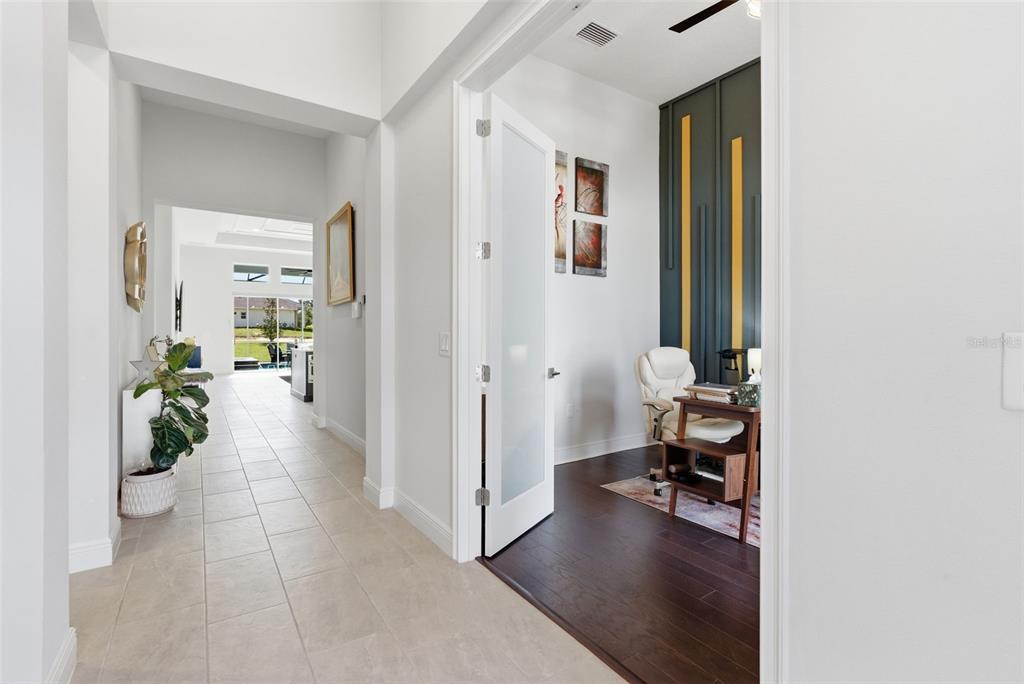 A hallway with tile flooring leads to a home office featuring dark wood floors — 13444 TRAILING MOSS DRIVE, DADE CITY, FL