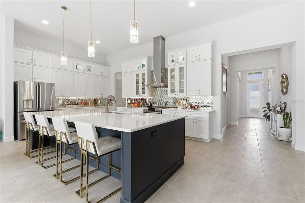 A modern kitchen features white cabinetry, a dark blue island, and gold-accented bar stools — 13444 TRAILING MOSS DRIVE, DADE CITY, FL