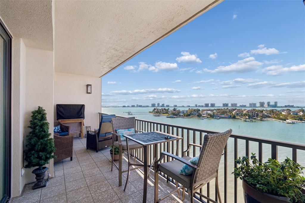 A balcony with two chairs and a table overlooks a bay and distant buildings — 4 BELLEVIEW BOULEVARD UNIT 701, BELLEAIR, FL