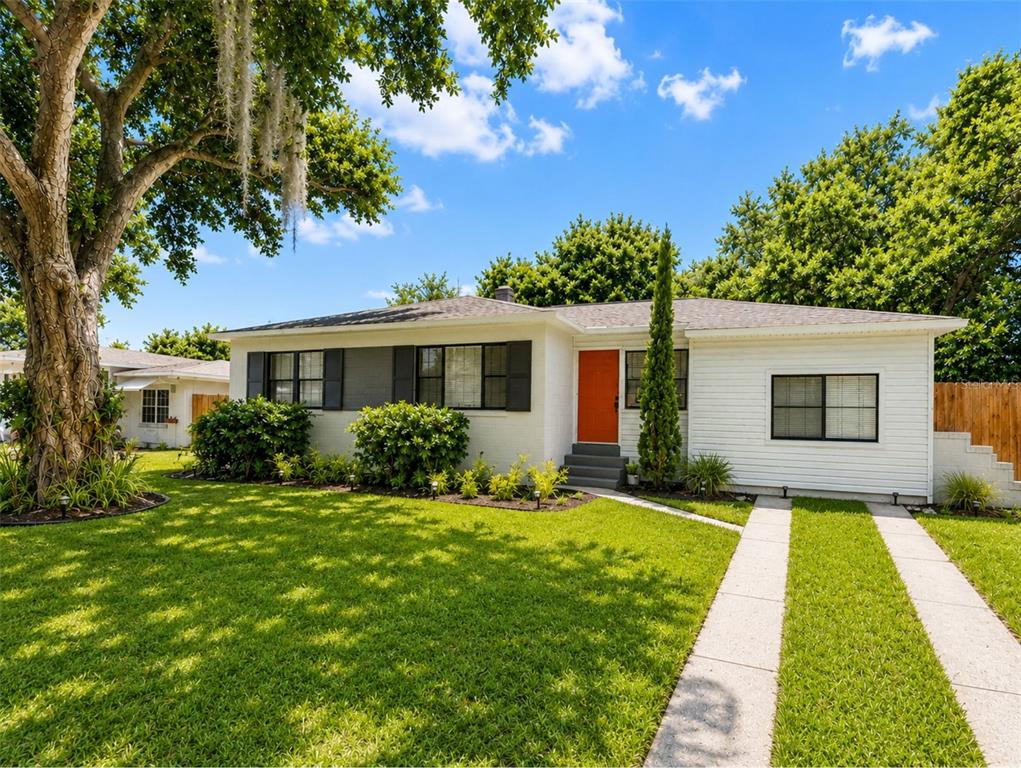 A white single-story house with a bright orange front door and a concrete driveway — 1330 MONTEREY DRIVE, EUSTIS, FL