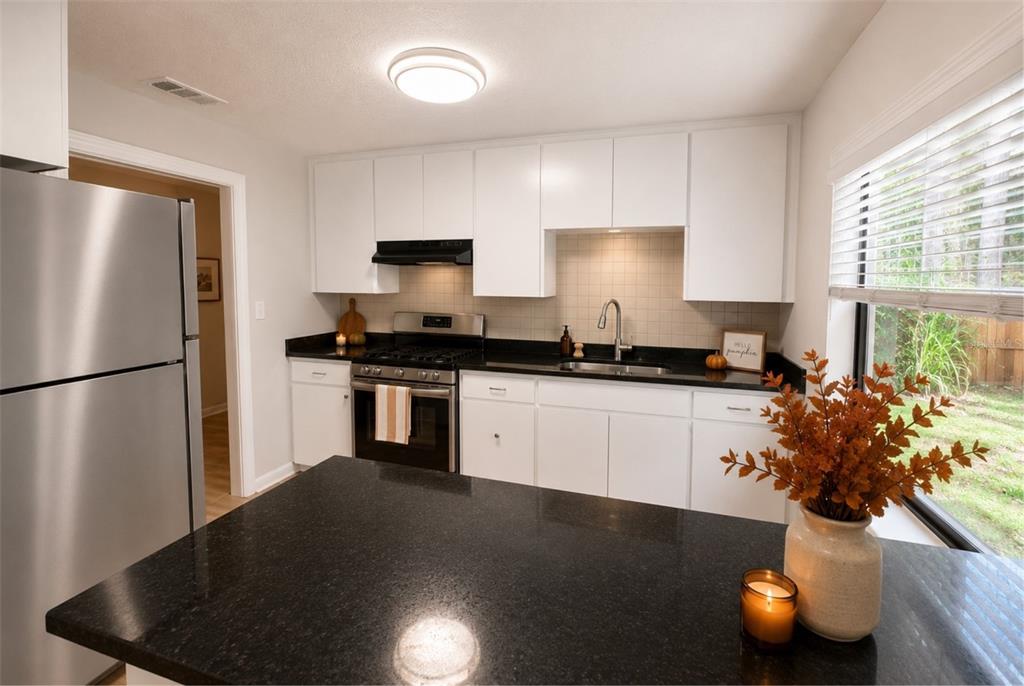 A kitchen features white cabinets, black countertops, stainless steel appliances, and a window with blinds — 1330 MONTEREY DRIVE, EUSTIS, FL