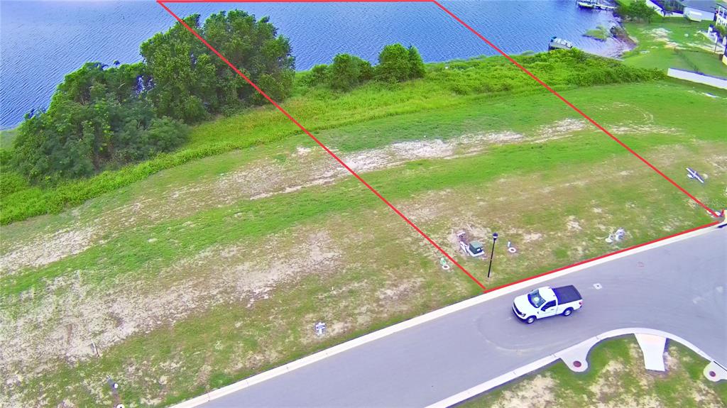 An aerial view shows a vacant waterfront residential lot outlined in red next to a road — 4389 JULIANA LAKE DRIVE, AUBURNDALE, FL
