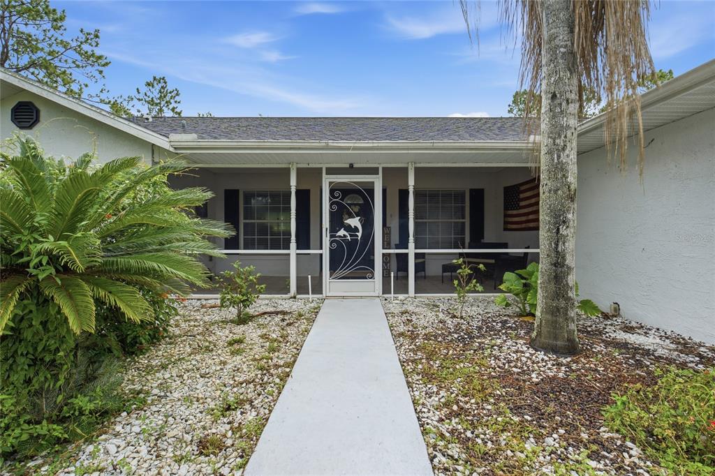 A covered front porch features a black door, tiled flooring, and outdoor seating furniture — 4353 W PINE RIDGE BOULEVARD, BEVERLY HILLS, FL
