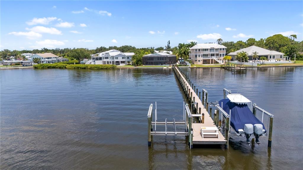 A long wooden dock extends into the water toward several waterfront houses and a boat — 818 NANCY GAMBLE LANE, ELLENTON, FL