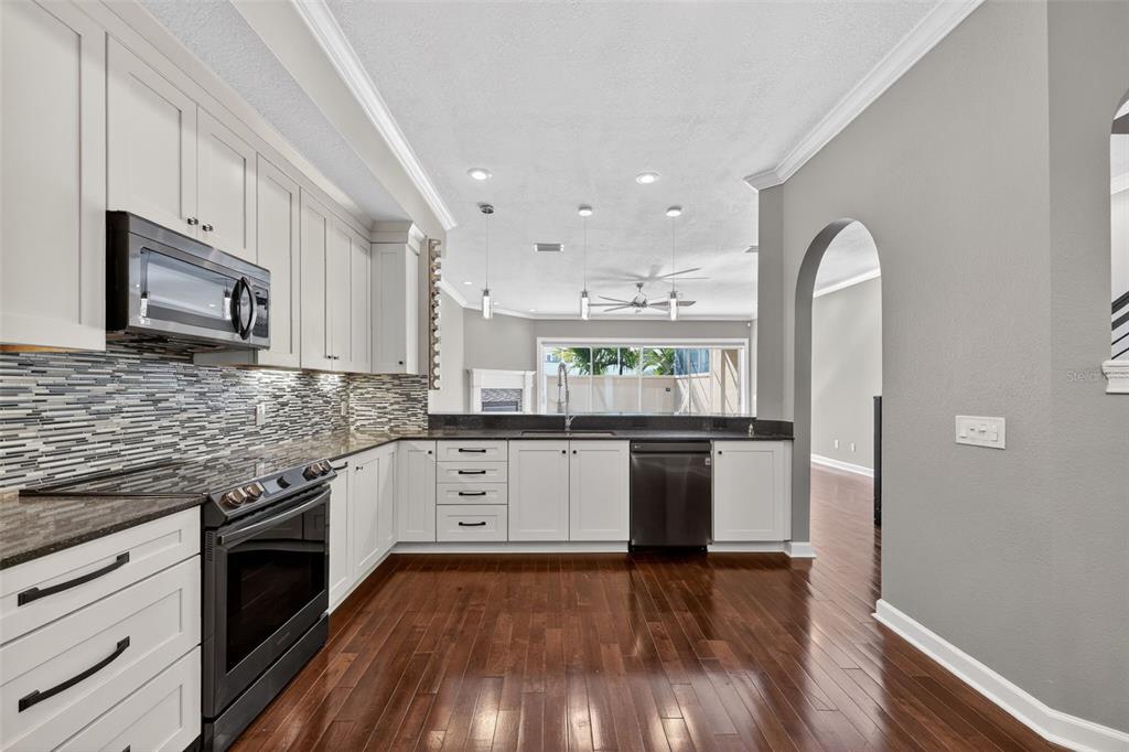 A kitchen with white cabinets, dark countertops, a tiled backsplash, and hardwood flooring — 348 LARBOARD WAY, CLEARWATER BEACH, FL