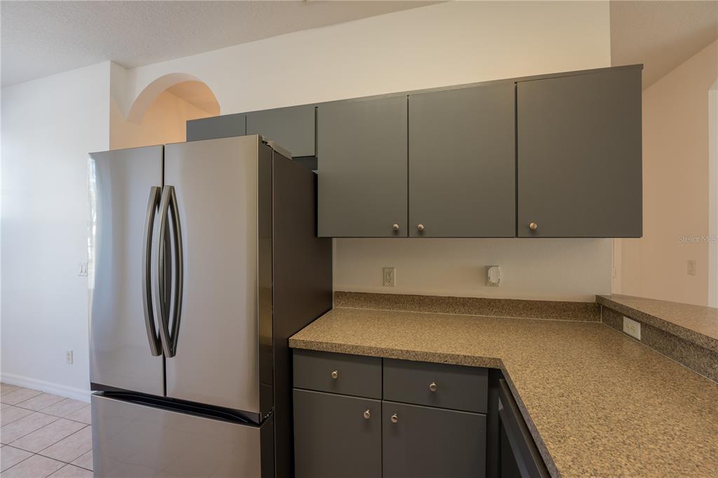 A stainless steel refrigerator stands next to dark gray cabinets and a speckled countertop — 4712 HEMINGWAY HOUSE STREET, KISSIMMEE, FL