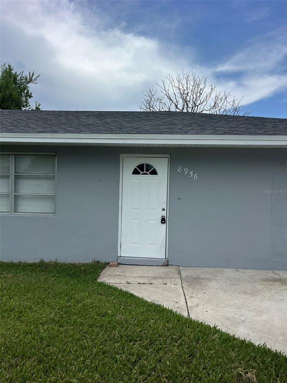 A gray house exterior features a white front door and a concrete walkway — 8956 SE 65TH WAY, OKEECHOBEE, FL