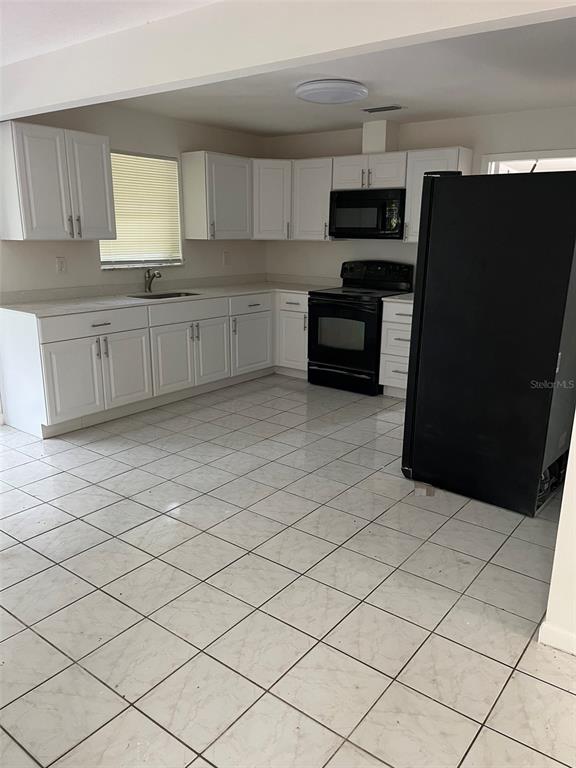 A kitchen features white cabinets, black appliances, and light-colored tiled flooring — 8956 SE 65TH WAY, OKEECHOBEE, FL