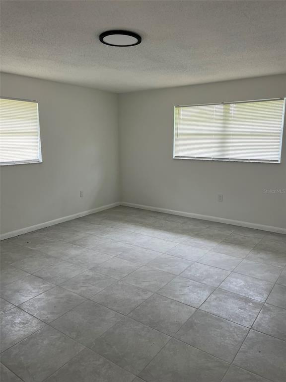 An empty room features light gray tile flooring, white walls, and two windows with blinds — 8956 SE 65TH WAY, OKEECHOBEE, FL