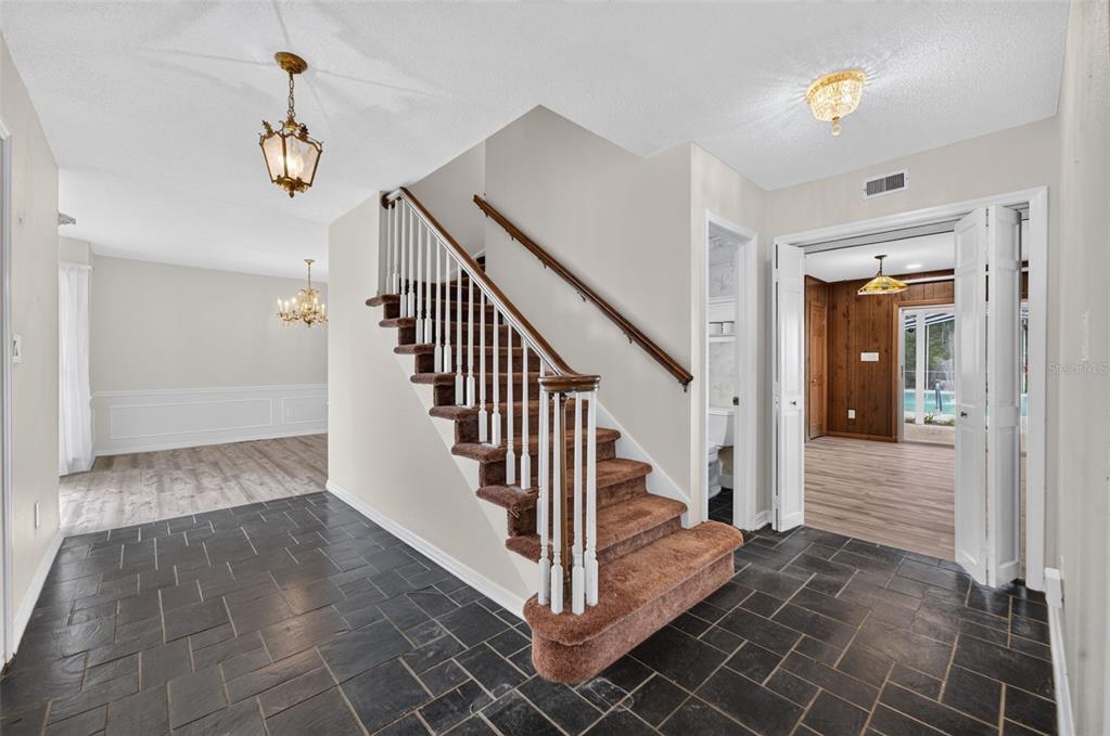 A foyer with dark slate tile flooring features a carpeted staircase and an adjacent room — 60 OAKLEIGH LANE, MAITLAND, FL