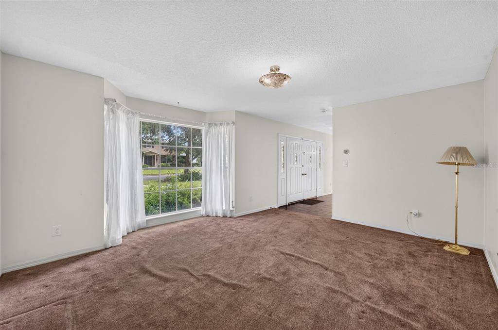 A carpeted living room features a bay window with white curtains and a floor lamp — 60 OAKLEIGH LANE, MAITLAND, FL