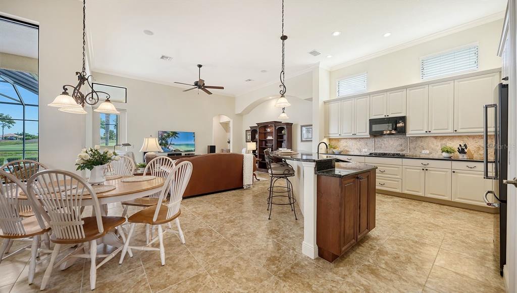 An open-concept kitchen and dining area features tile flooring, cream cabinetry, and a breakfast bar — 12717 STONE RIDGE PLACE, LAKEWOOD RANCH, FL