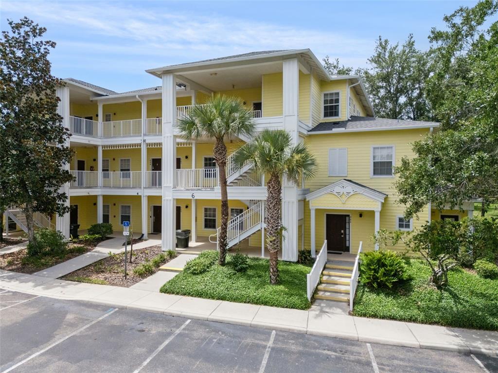 A three-story yellow apartment building with exterior staircases, balconies, and palm trees in front — 207 LUCAYA LOOP UNIT 207, DAVENPORT, FL