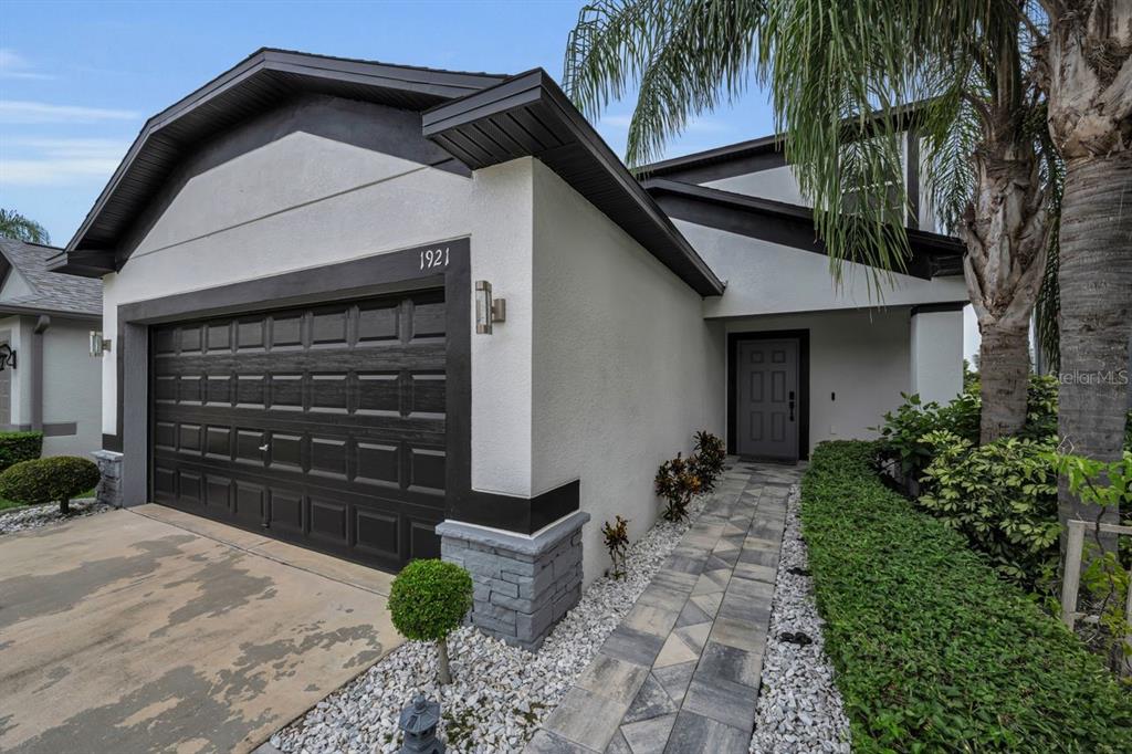 A two-story suburban house features a dark garage door, white stucco walls, and landscaped hedges — 1921 HAWKS VIEW DRIVE, RUSKIN, FL