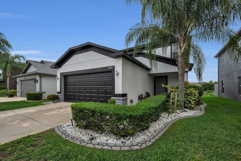 A modern house exterior features a dark garage door, stone accents, and a paved walkway — 1921 HAWKS VIEW DRIVE, RUSKIN, FL