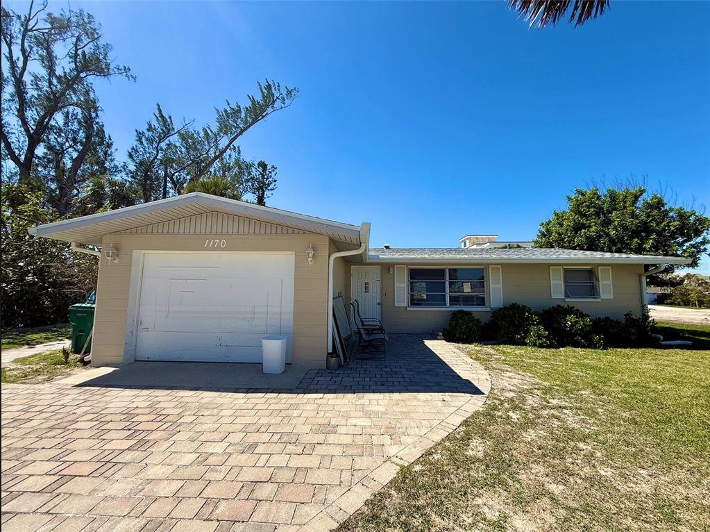 A single-story house with a tan exterior, a white garage door, and a paved driveway — 1170 LITTLE COURT, ENGLEWOOD, FL