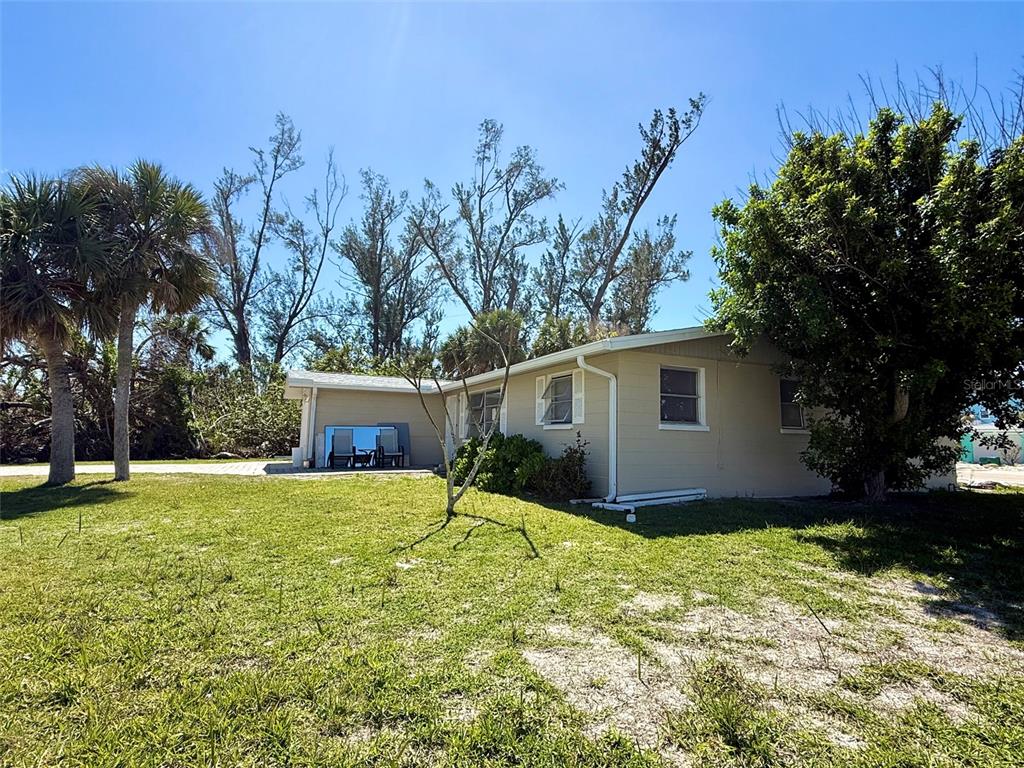 A single-story tan house with a small patio sits on a grassy lot with trees — 1170 LITTLE COURT, ENGLEWOOD, FL