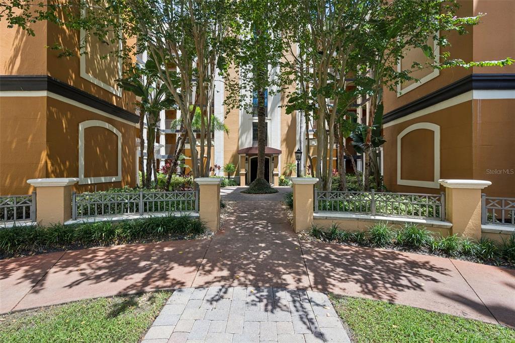 A paved walkway leads to the entrance of a multi-story apartment building with tan walls — 12539 FLORIDAYS RESORT DRIVE UNIT 102D, ORLANDO, FL