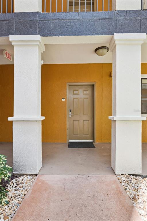 A tan front door is centered between two white pillars on a covered concrete porch — 12539 FLORIDAYS RESORT DRIVE UNIT 102D, ORLANDO, FL