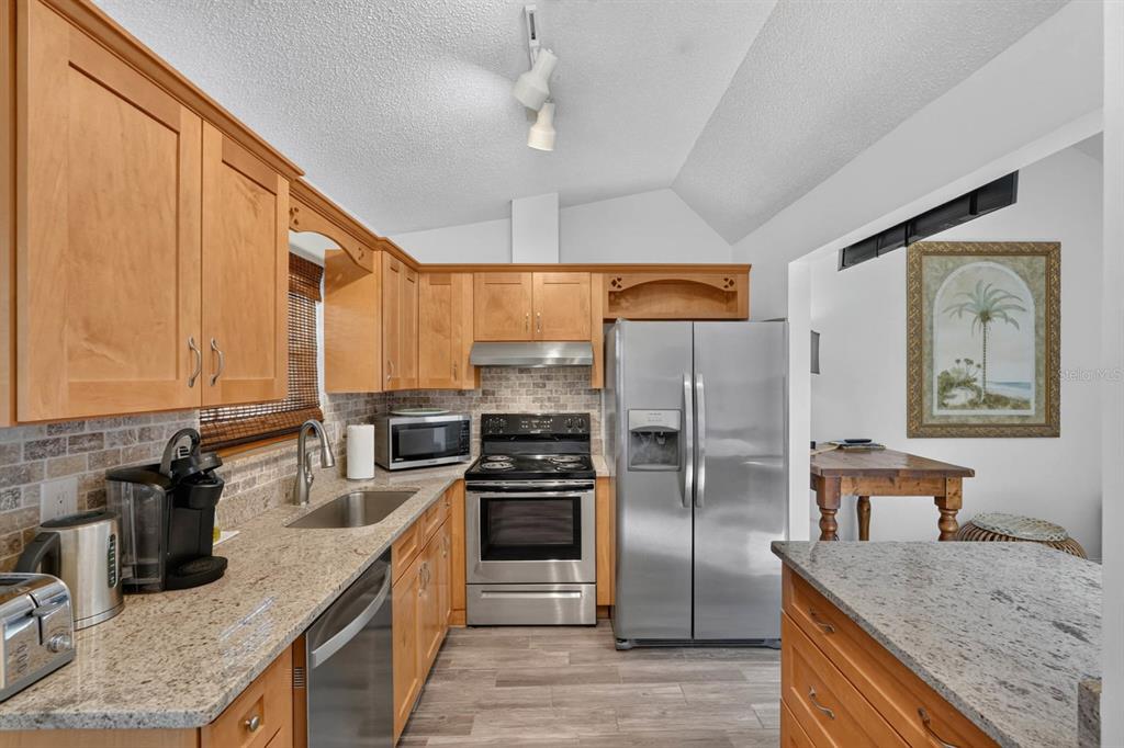 A kitchen features light wood cabinets, granite countertops, stainless steel appliances, and a vaulted ceiling — 5 ARBOR LAKE PARK, ORMOND BEACH, FL