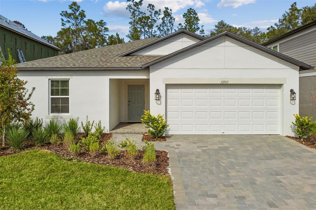 A single-story house with a white stucco exterior, a paved driveway, and a two-car garage — 12915 CASTLE OAKS DRIVE, HUDSON, FL
