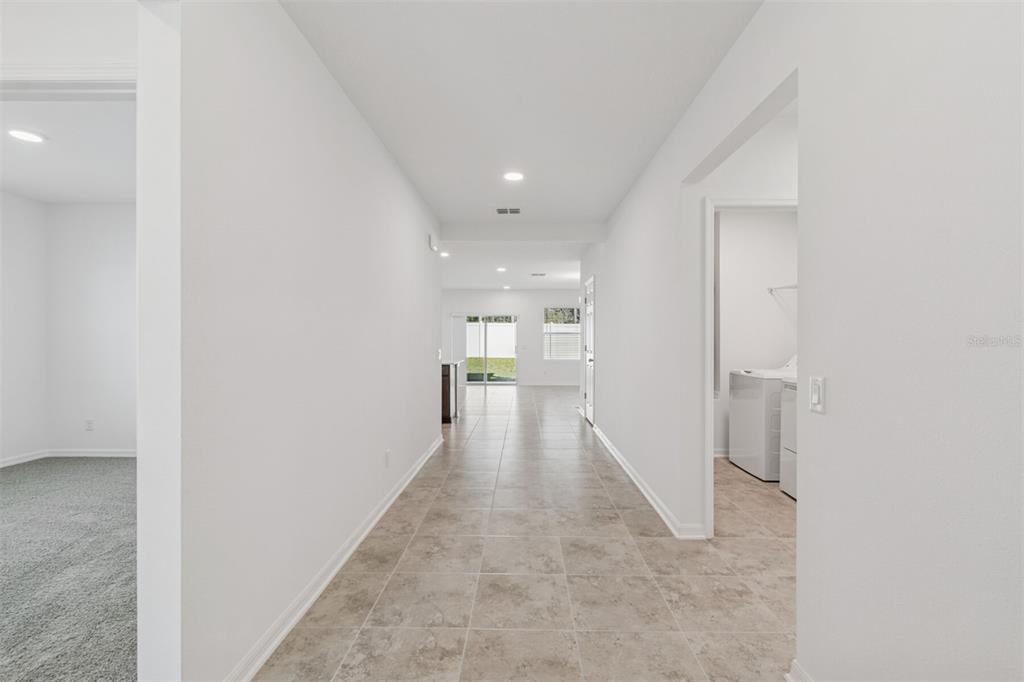 A tiled hallway leads past a laundry room toward an open living area with glass doors — 12915 CASTLE OAKS DRIVE, HUDSON, FL