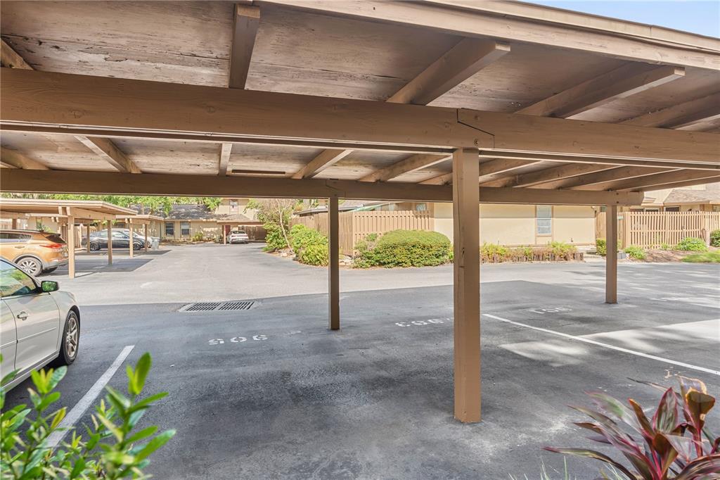 A covered parking area with wooden support beams and marked asphalt spaces — 903 BUCK COURT, BRANDON, FL