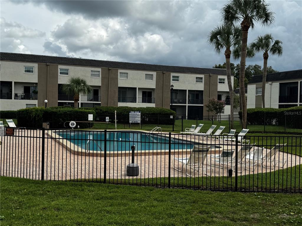 A swimming pool with lounge chairs is enclosed by a black metal fence near apartments — 706 OAKGROVE DRIVE UNIT 114, BRANDON, FL